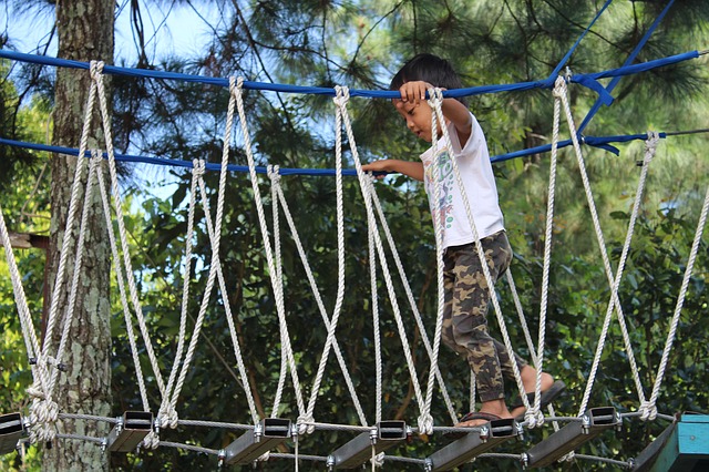 A little boy traveling across a bridge held up by ropes.